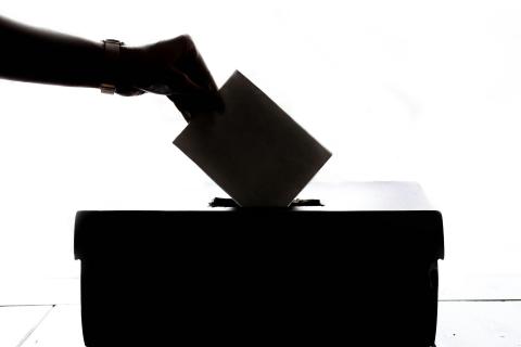 A silhouette of a hand putting a folded paper into a ballot box